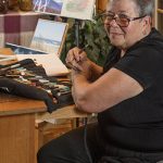 Liisa Trala, Osher Lifelong Learning Institute instructor sitting with brushes in front of a few paintings.