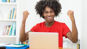 High school student sitting at laptop raising two fists in celebration