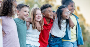 Inclusive group of smiling children standing together with arms linked.