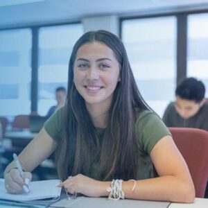 Young woman writing in notebook at a table, smiling